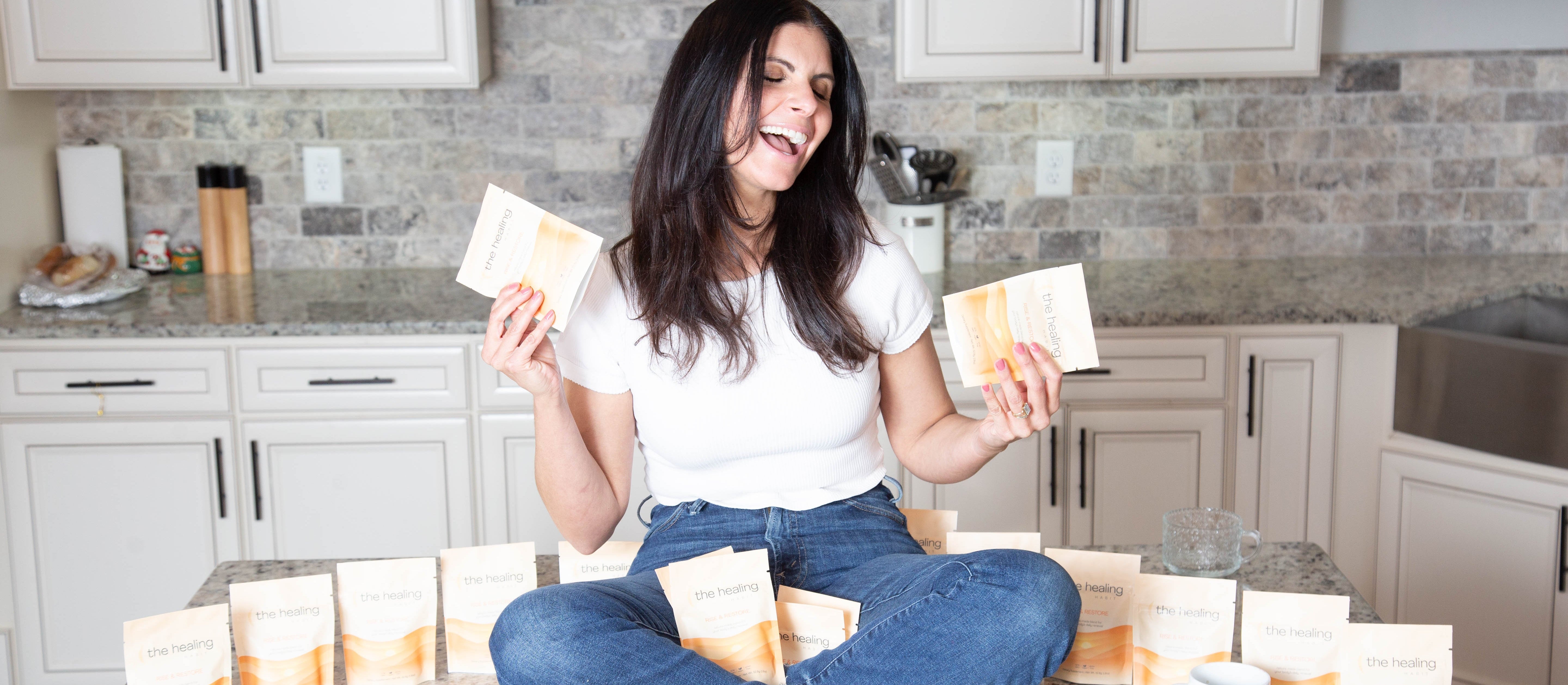 Woman sitting on a kitchen counter holding packages, with more packages on the counter.